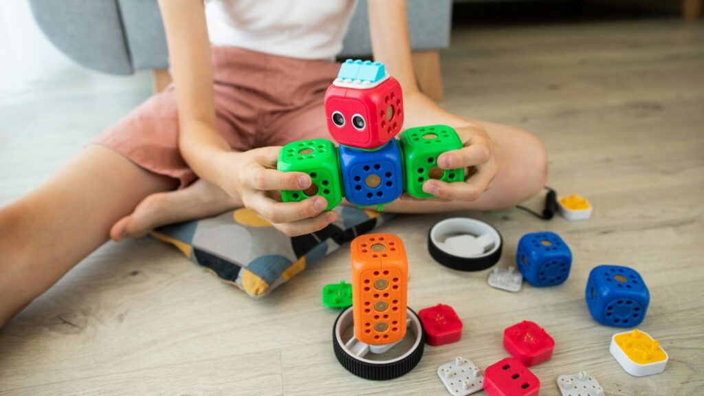Mans d'una nena muntant un petit robot amb mòduls de colors, asseguda a terra
