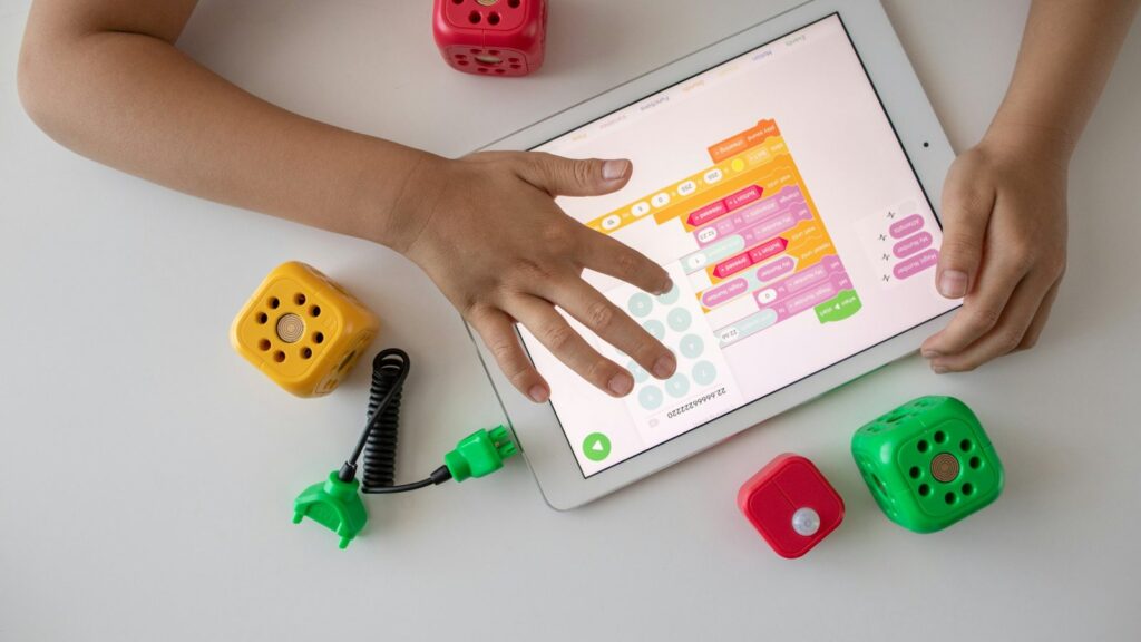 Mans d'un infant programant amb blocs de colors en una tauleta, al costat de mòduls de robòtica